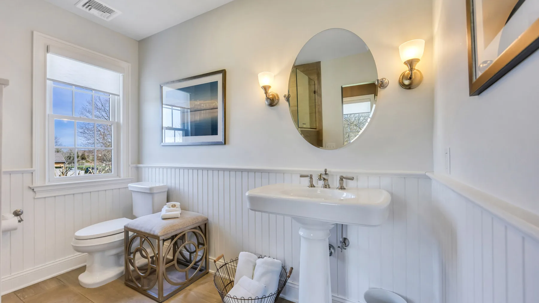 Un baño con lavabo de pedestal, inodoro y espejo ovalado.