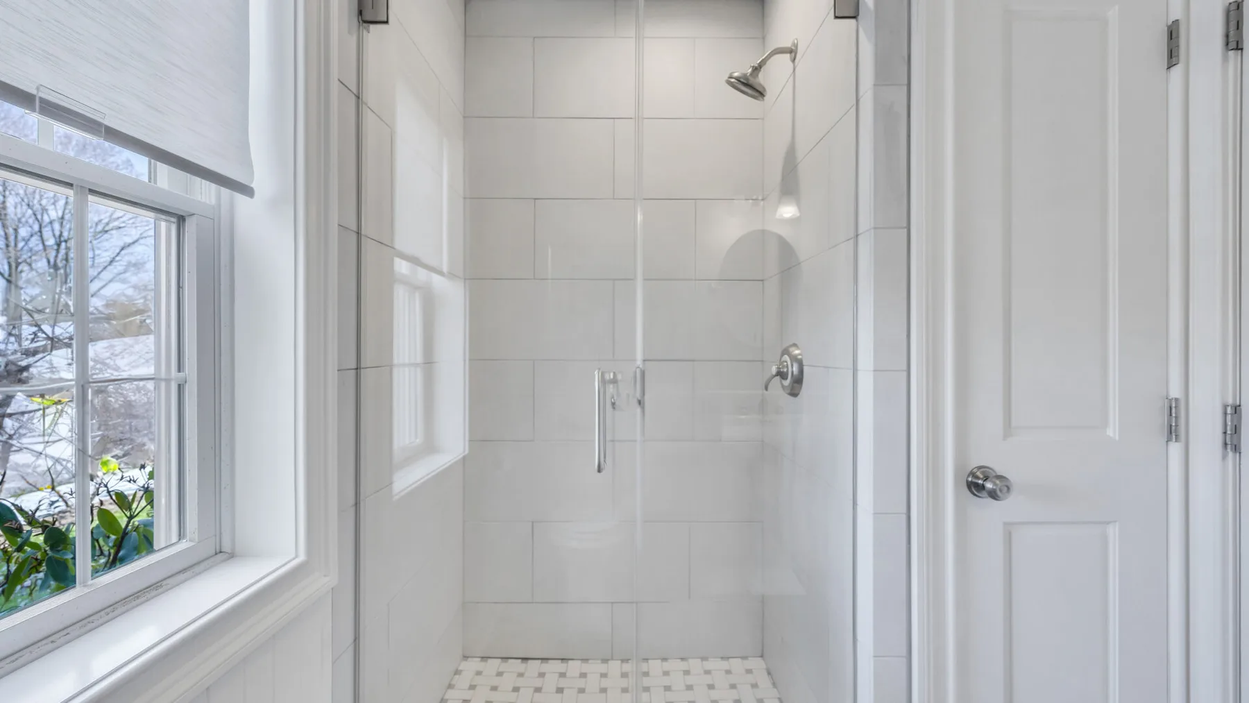 Un baño luminoso con una ducha de vidrio junto a una ventana.