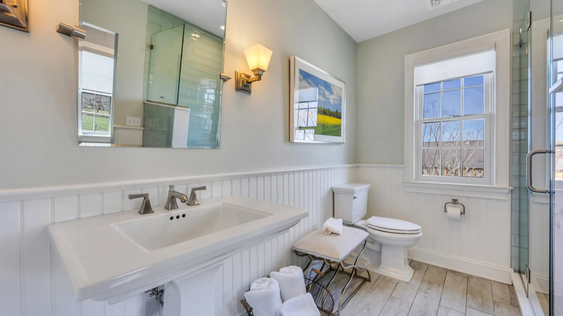Un baño luminoso con un lavabo largo, inodoro y ducha de vidrio.