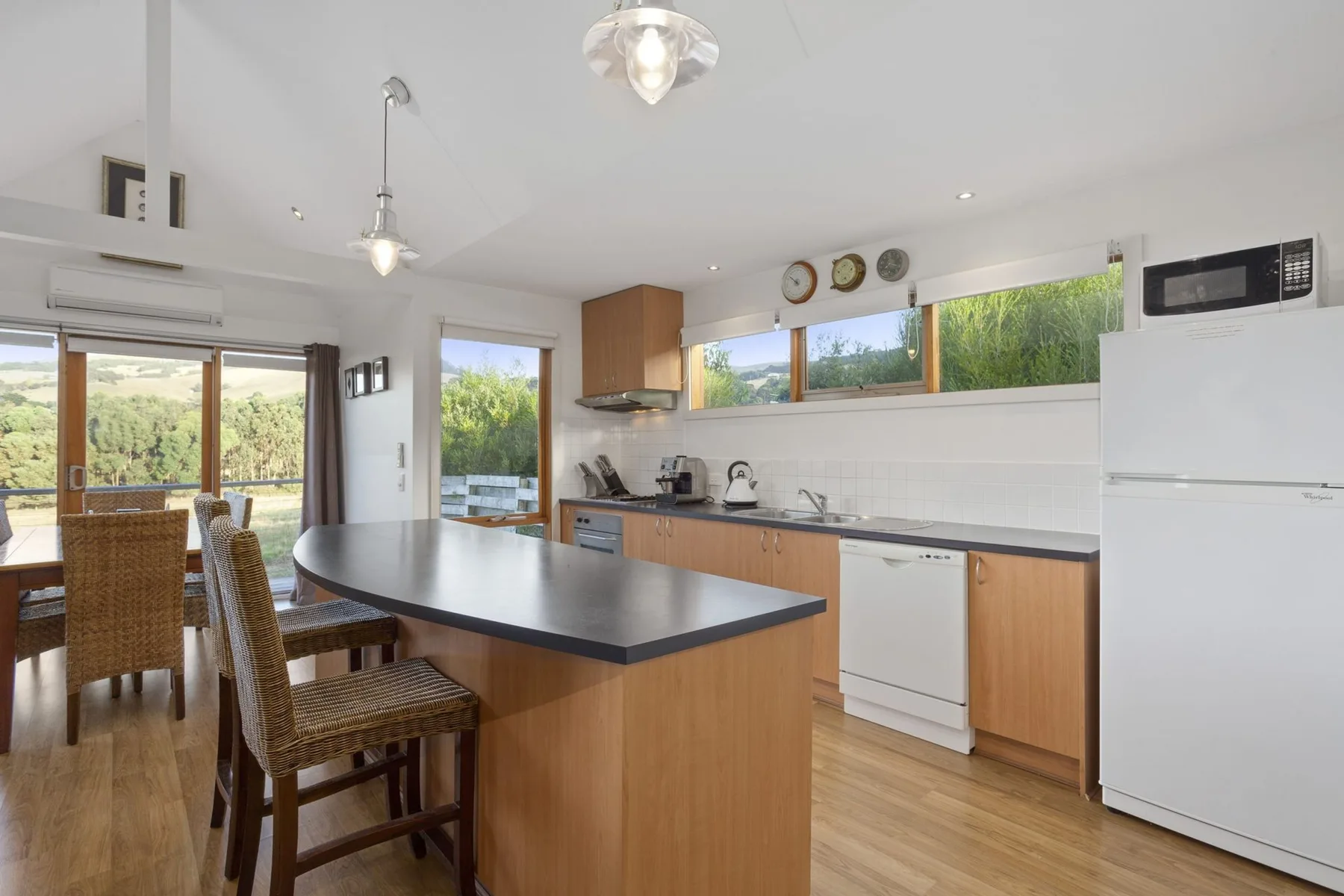A bright kitchen and dining area with a central island and windows overlooking greenery.