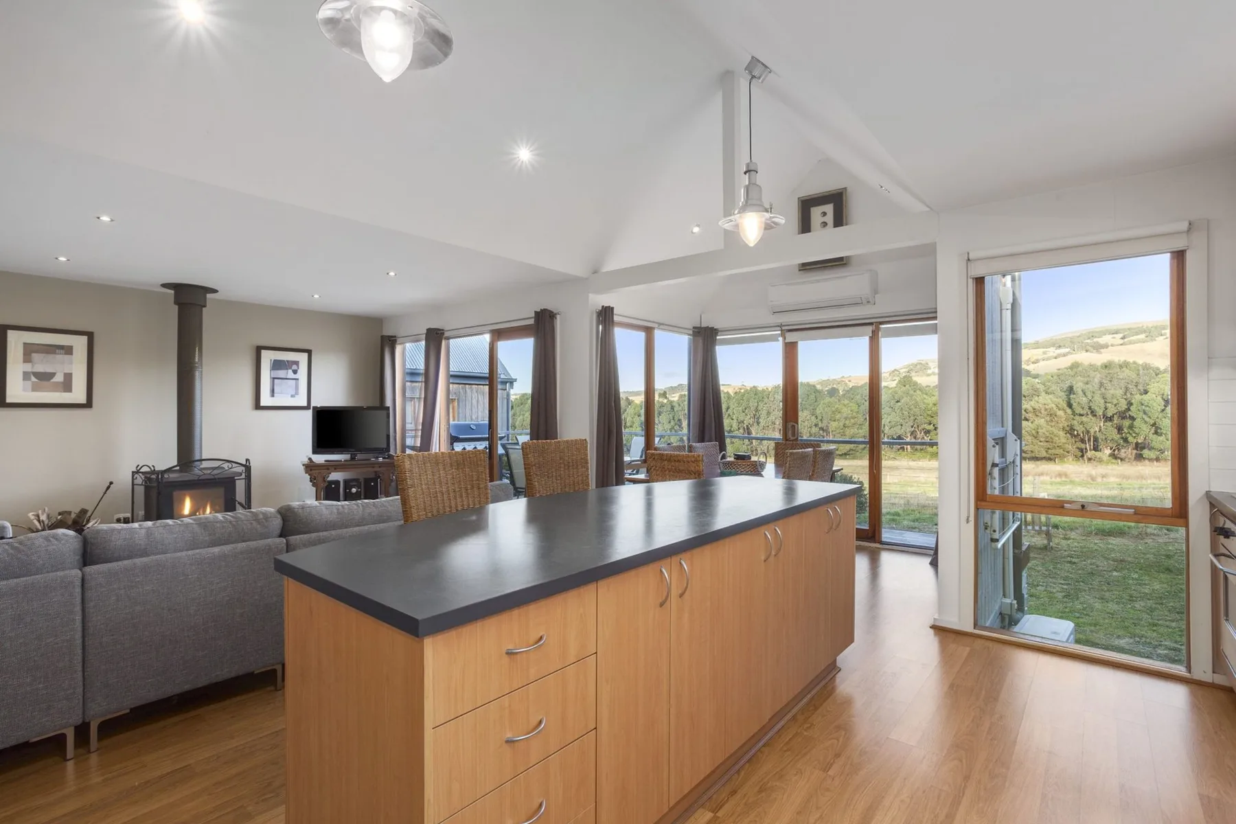 Open-plan living area with a kitchen island and large windows overlooking greenery.