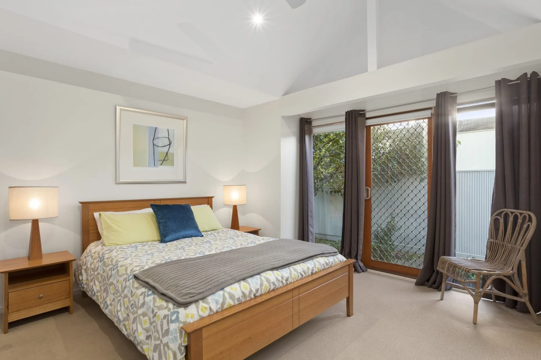 A bedroom with a double bed, bedside tables, and glass doors opening to a patio.
