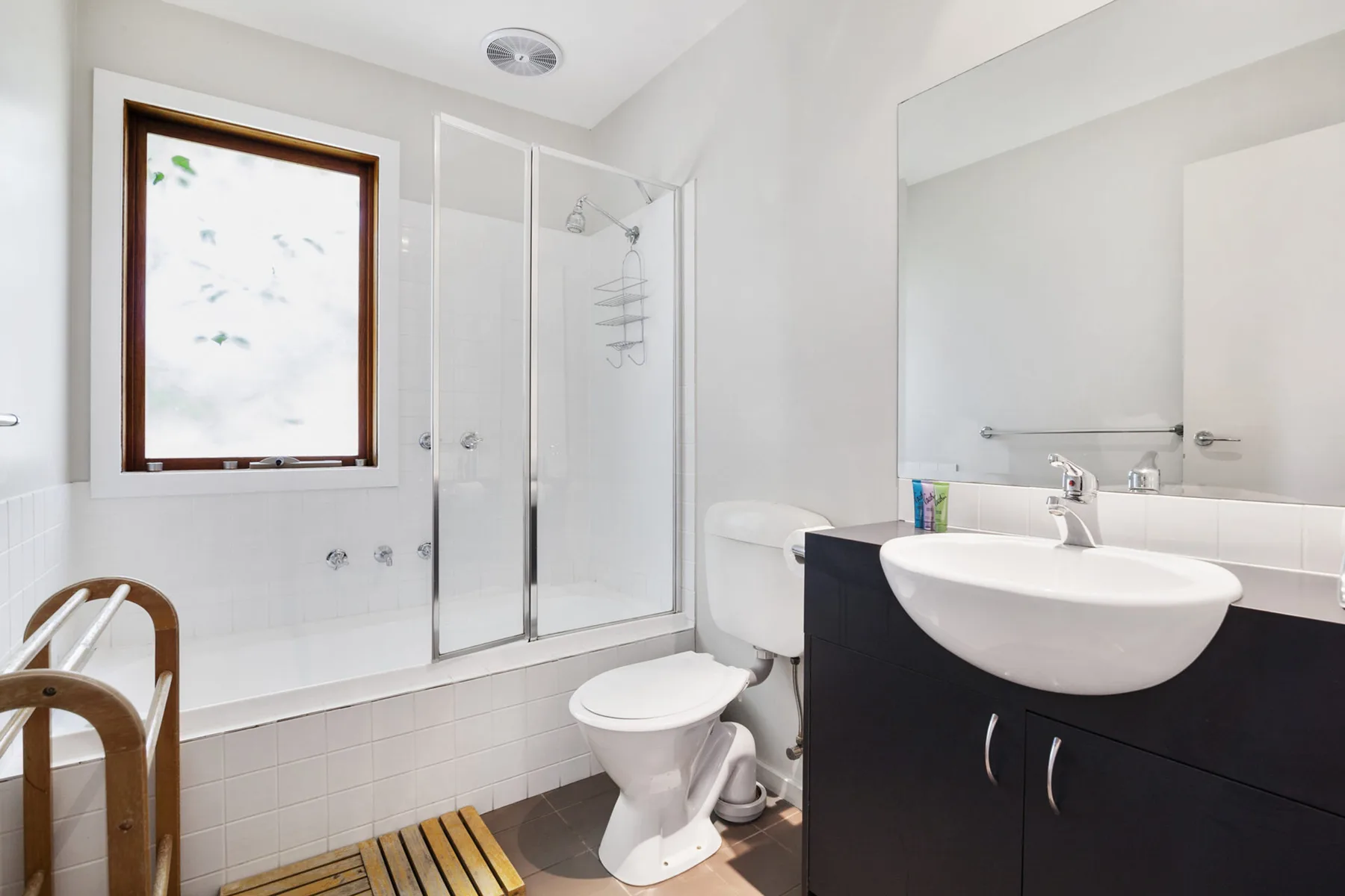 Baño luminoso con bañera, mampara de ducha y lavabo con mueble.