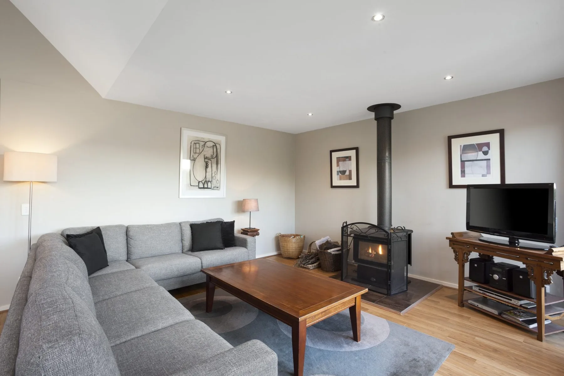 A living room with sectional seating, a coffee table, and a freestanding stove.