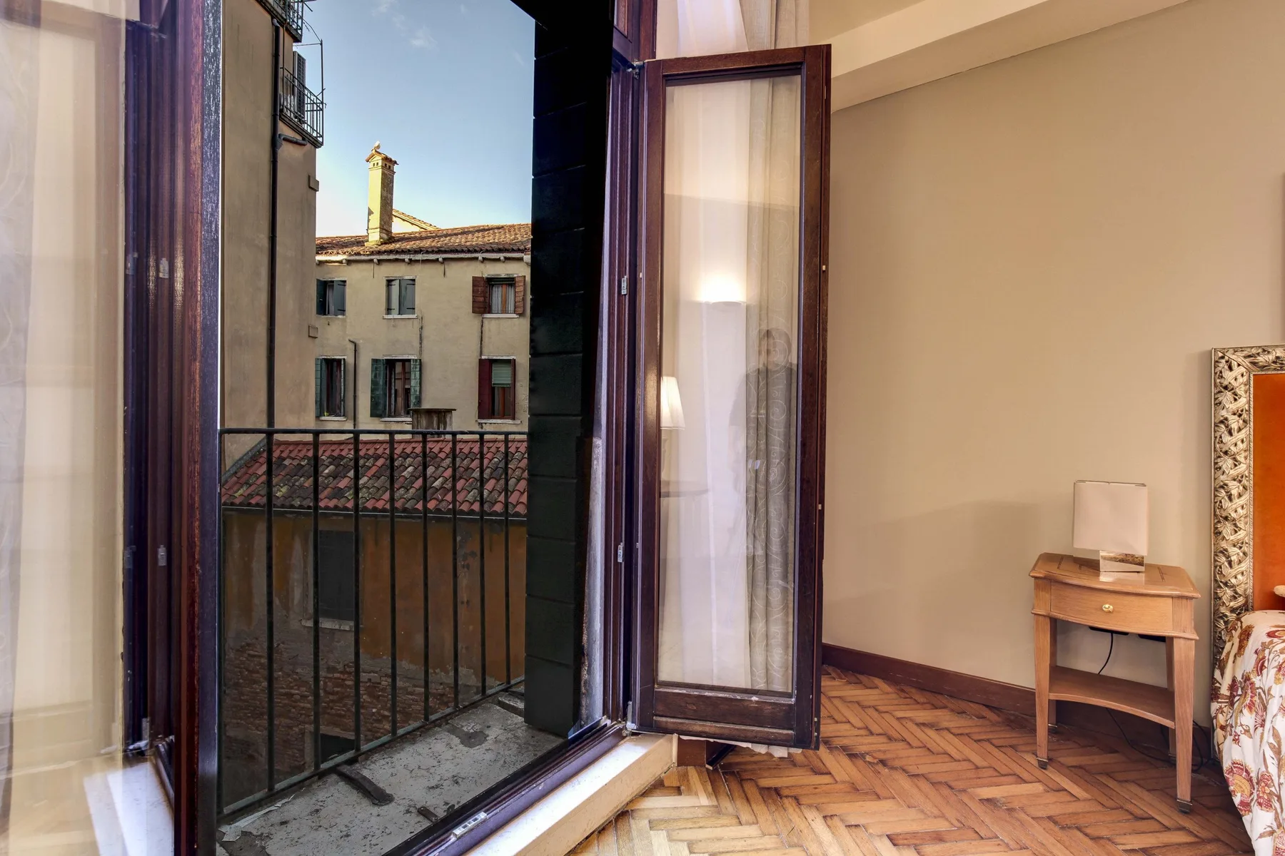 Una habitación se abre a un pequeño balcón por ventanas altas, con una mesita cercana.