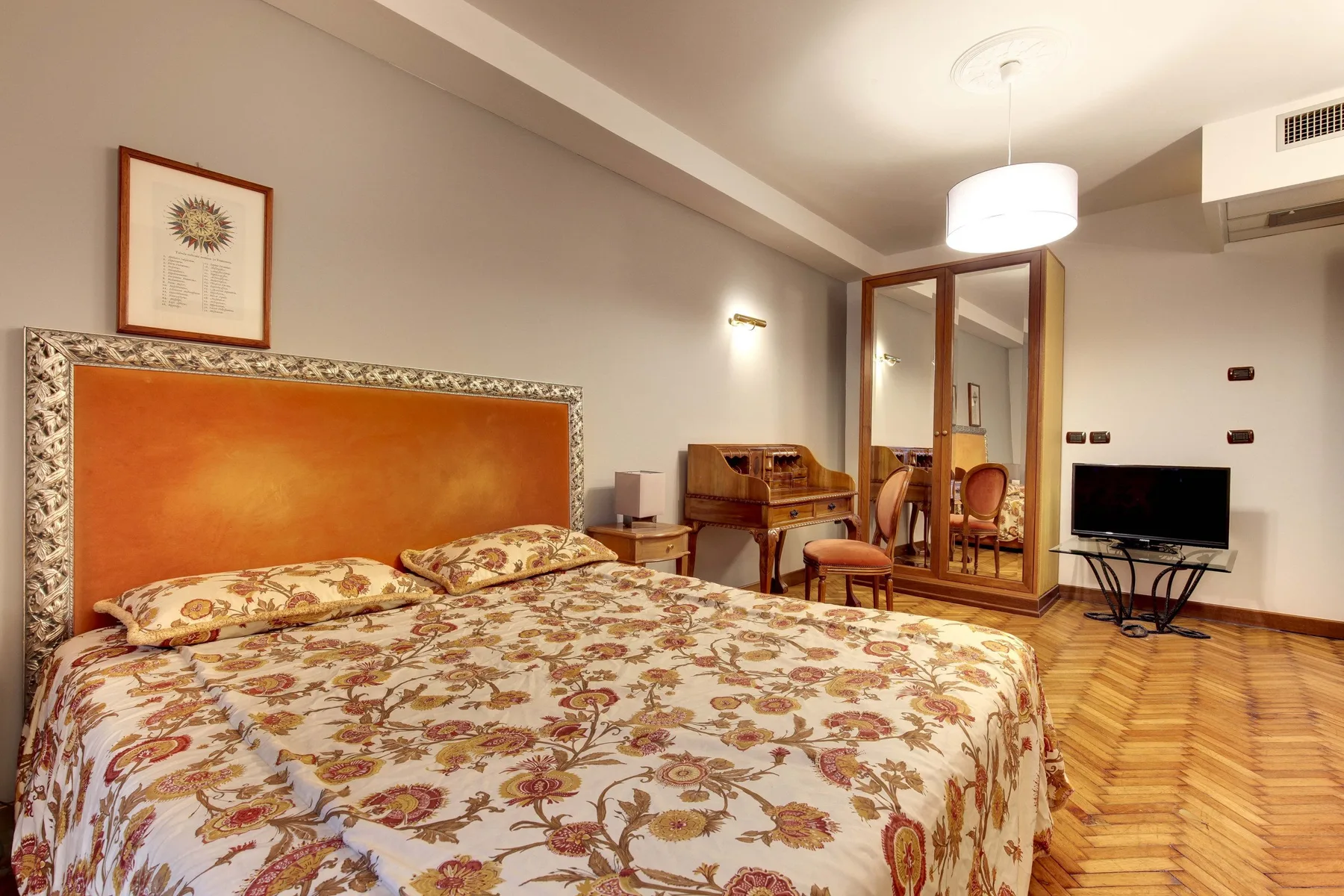 Un dormitorio con una colcha floral, un escritorio y un televisor.