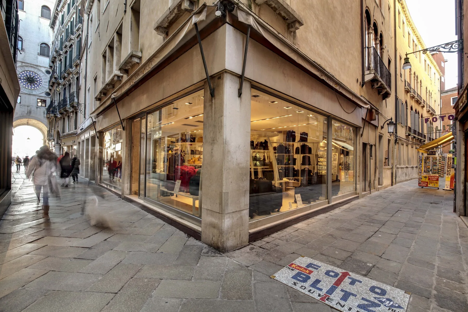 Una tienda de ropa ocupa la esquina de una calle estrecha pavimentada con piedra.