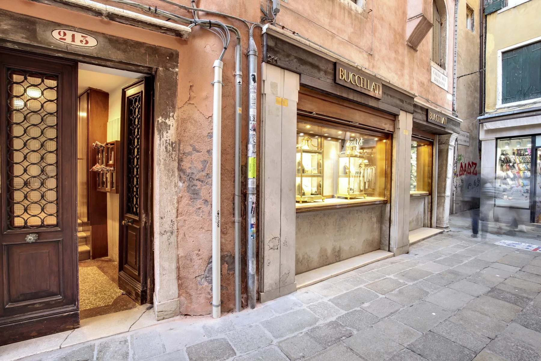 Una calle estrecha pavimentada con piedra, escaparates y una puerta abierta.