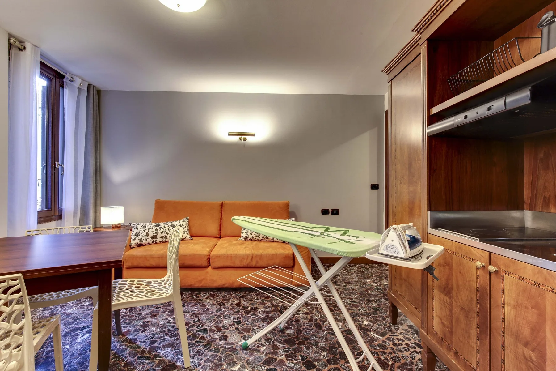 Una habitación amueblada con un sofá naranja, una mesa y una tabla de planchar.