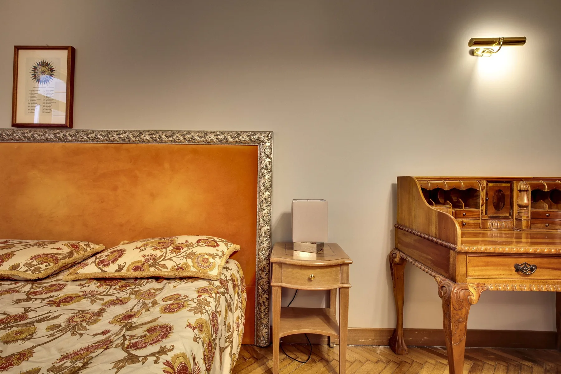 Un dormitorio con una cama estampada, una mesita de noche y un escritorio de madera.