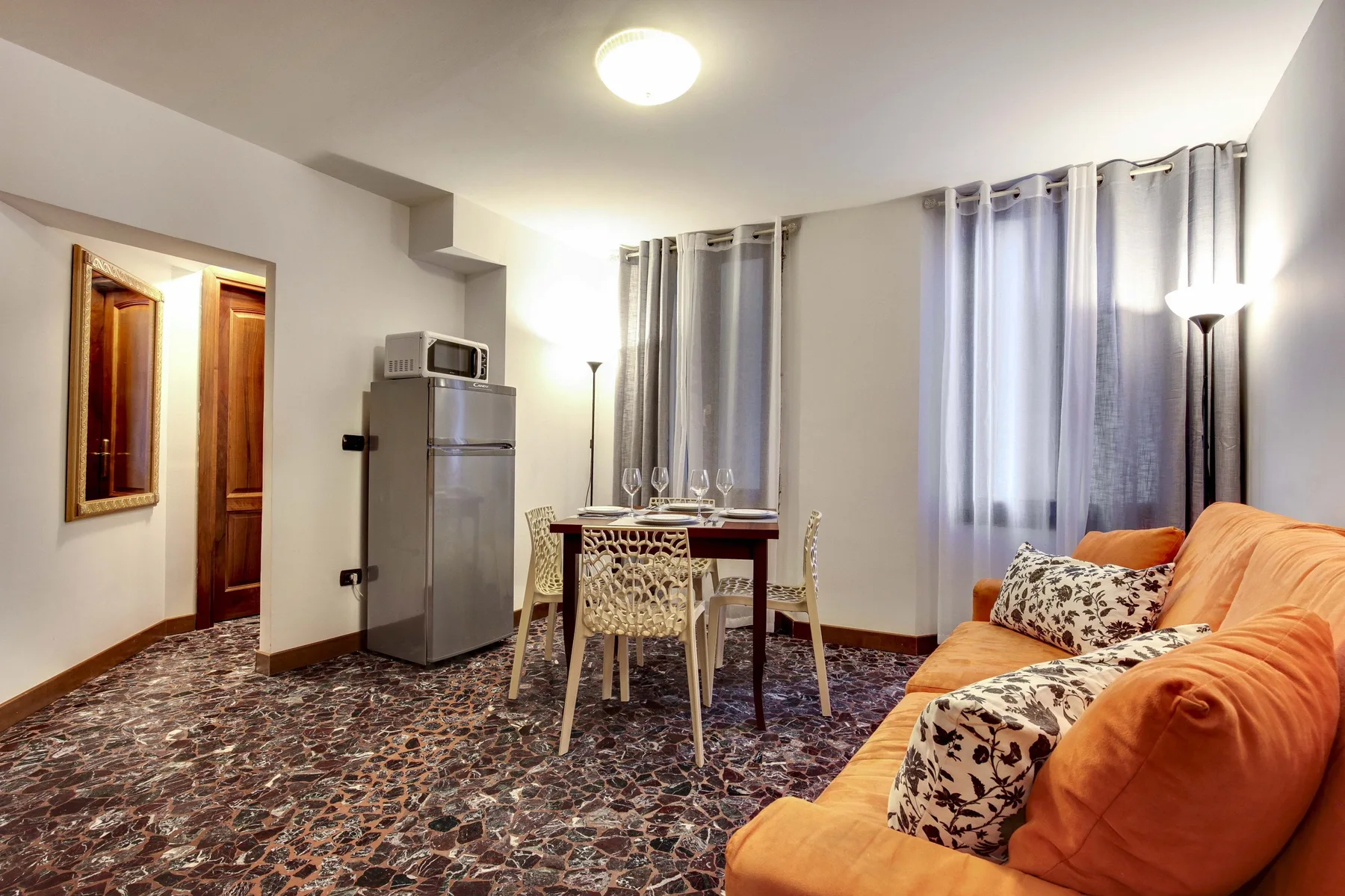 Una sala de estar con un sofá naranja, una mesa de comedor y ventanas con cortinas.
