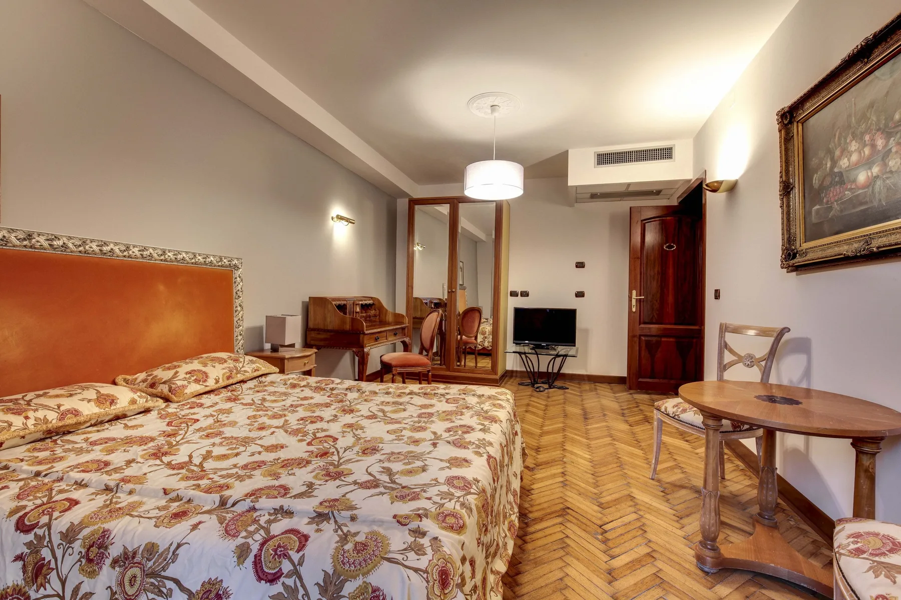 Un dormitorio con ropa de cama estampada, suelo de madera y una pequeña zona de estar.