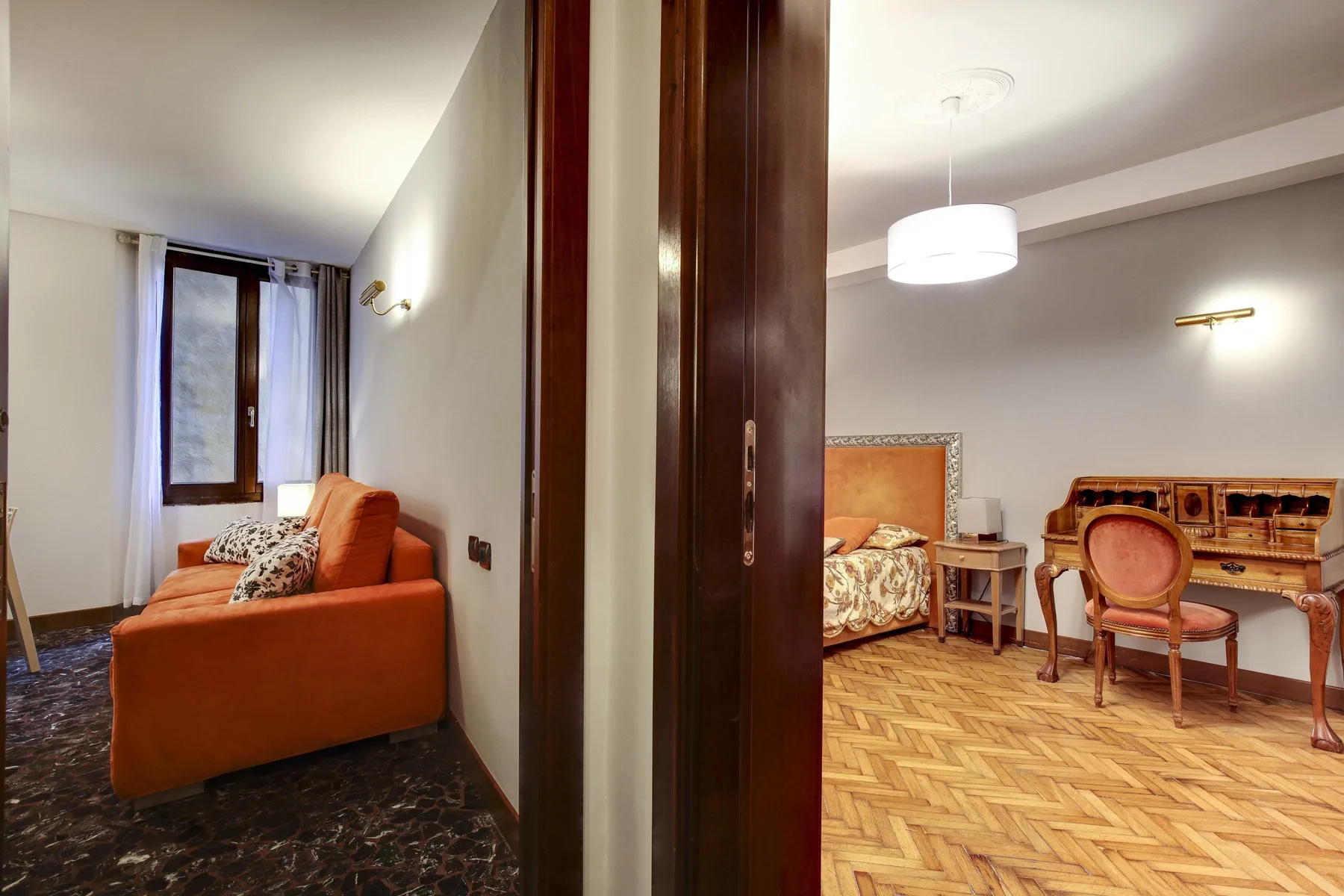 Se ven dos habitaciones amuebladas a través de una puerta, con asientos y una cama.