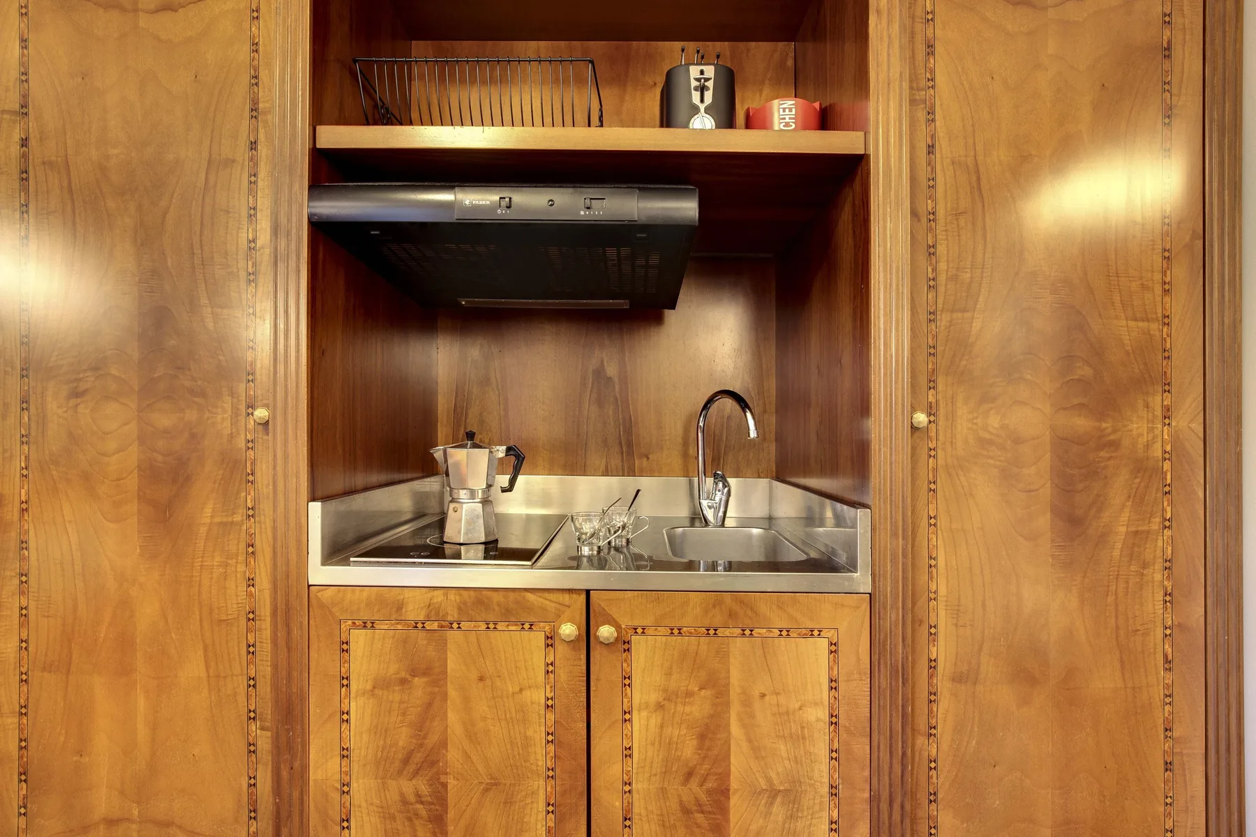 Una pequeña cocina con fregadero, grifo y placa de cocina bajo armarios de madera.