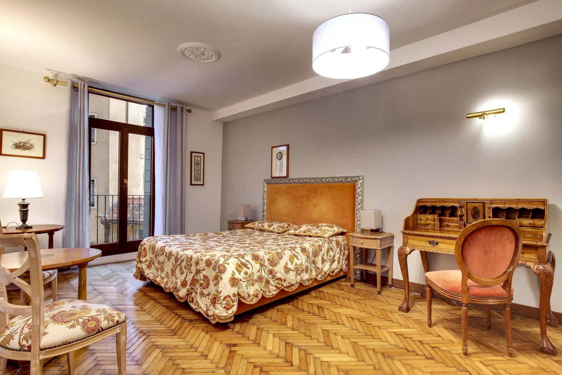 Un dormitorio con una colcha estampada, muebles de madera y puertas altas de vidrio.