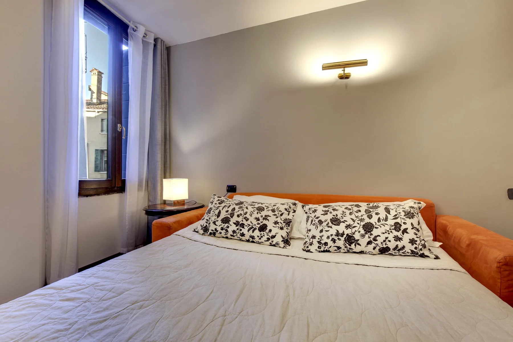 Un dormitorio con una cama, almohadas estampadas y una ventana junto a la cama.