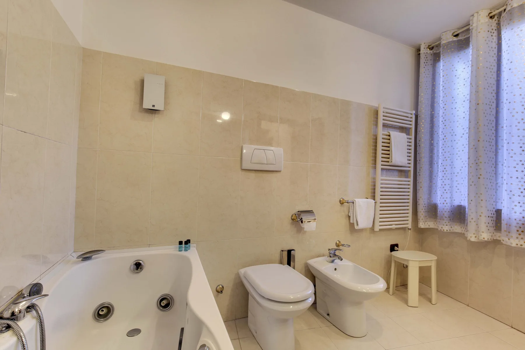 Un baño alicatado con bañera, inodoro, bidé y ventana con cortinas.