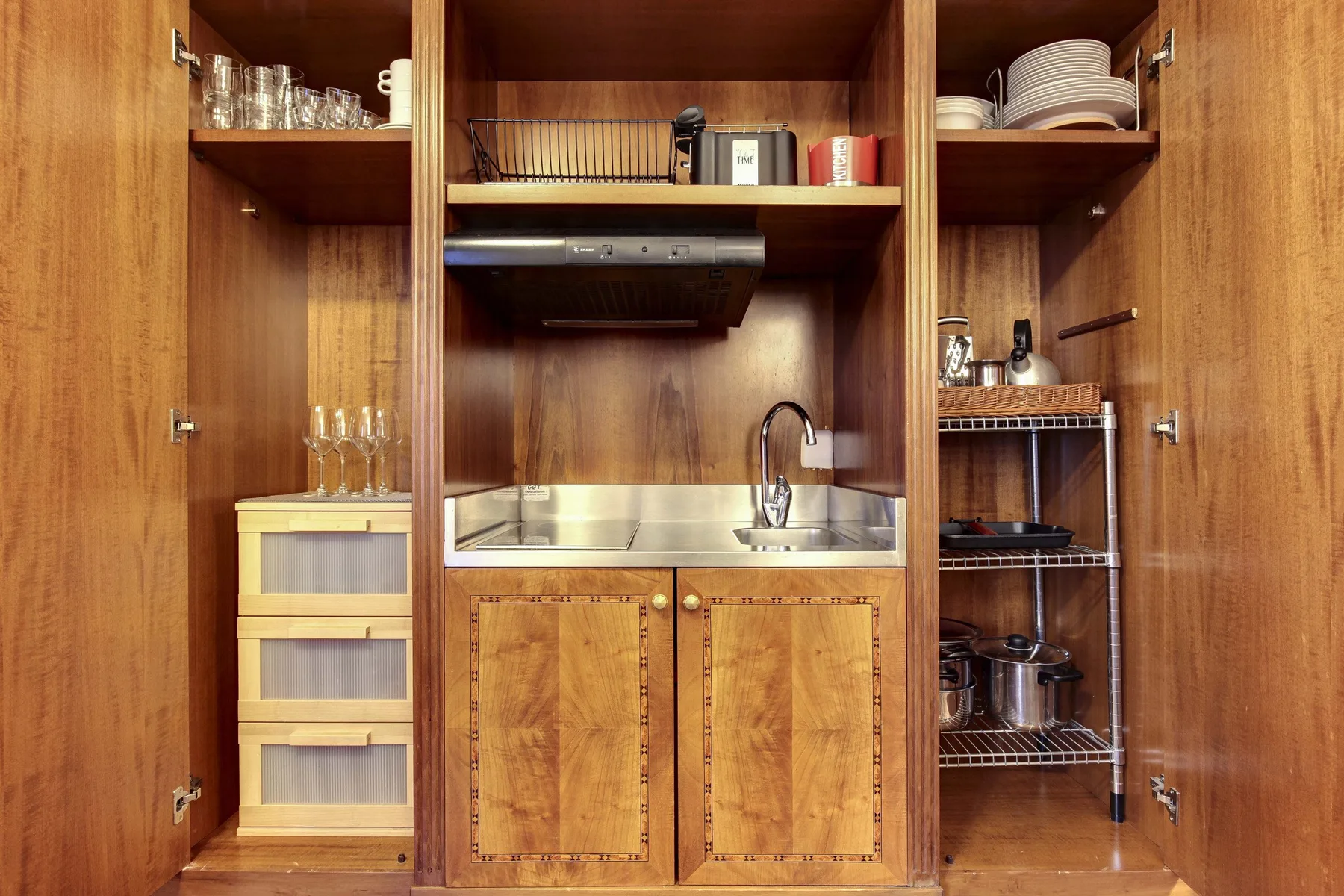 Una pequeña cocina de madera con fregadero, estantes abiertos y utensilios de cocina.