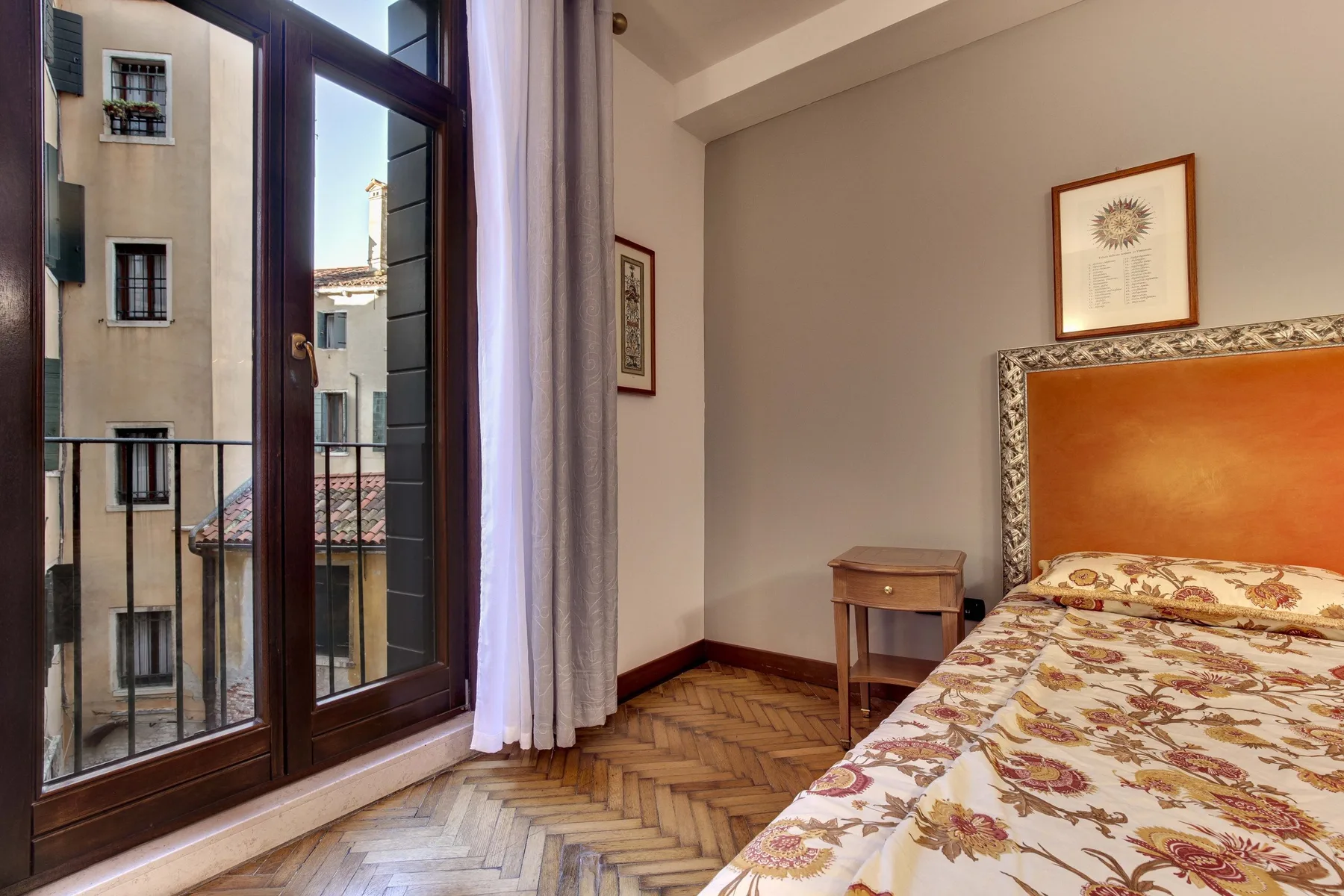 Un dormitorio con una colcha estampada junto a ventanas altas.