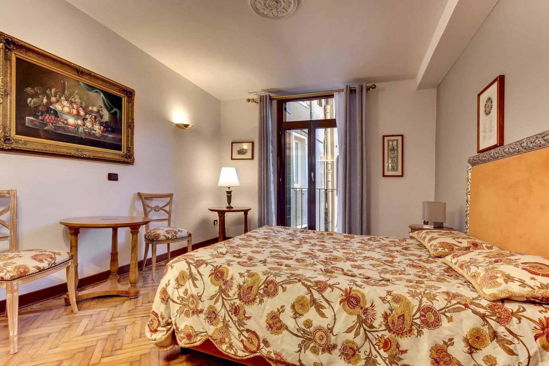 Un dormitorio con una cama cubierta de flores, una mesa pequeña y una puerta de cristal.