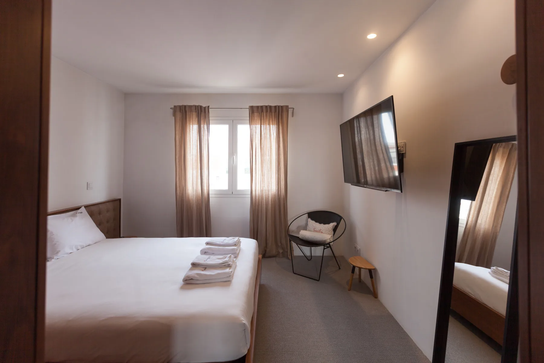 Un dormitorio con una cama, una ventana con cortinas y un televisor en la pared.