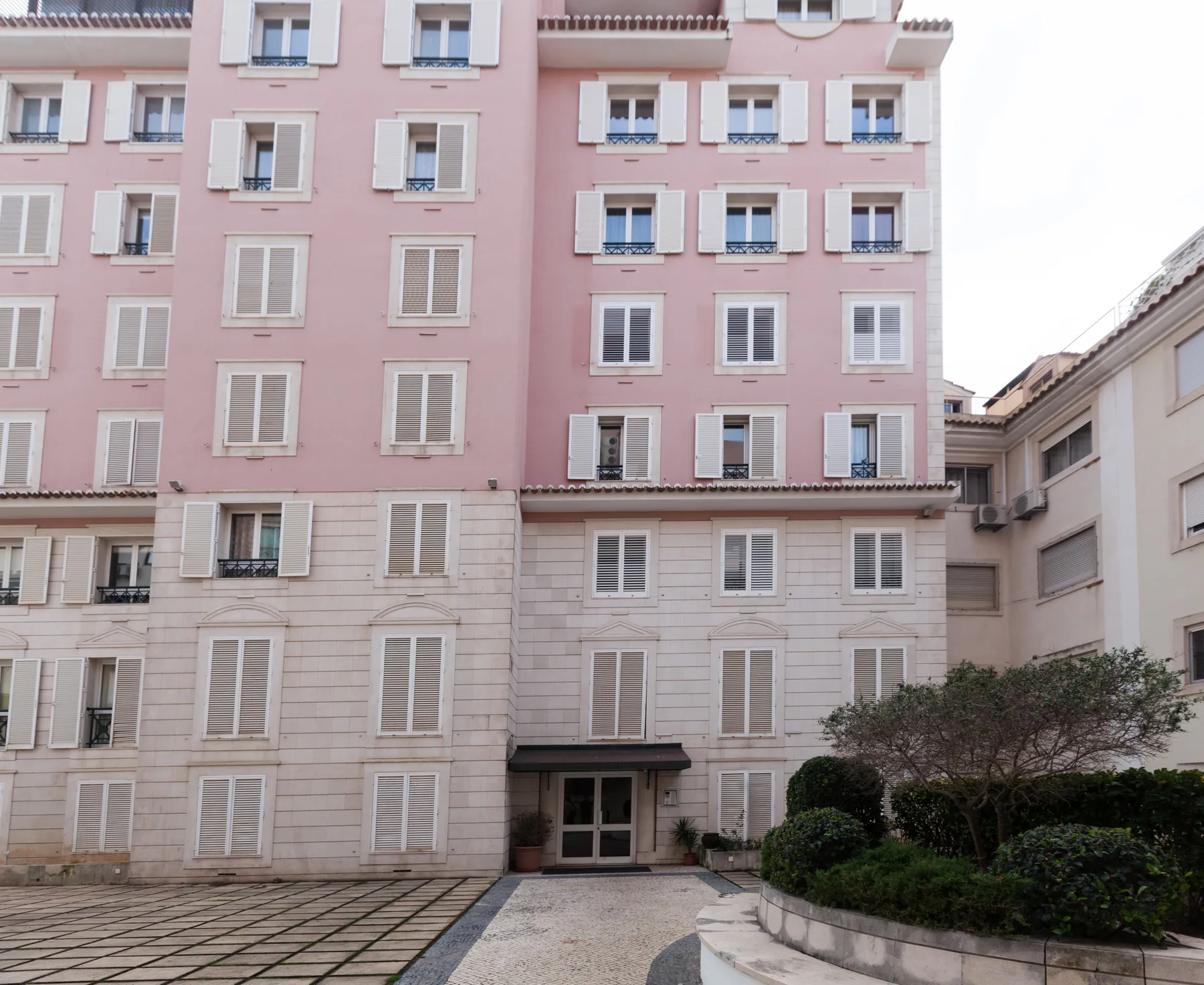 Un edificio de apartamentos rosa da a un patio pavimentado con arbustos.