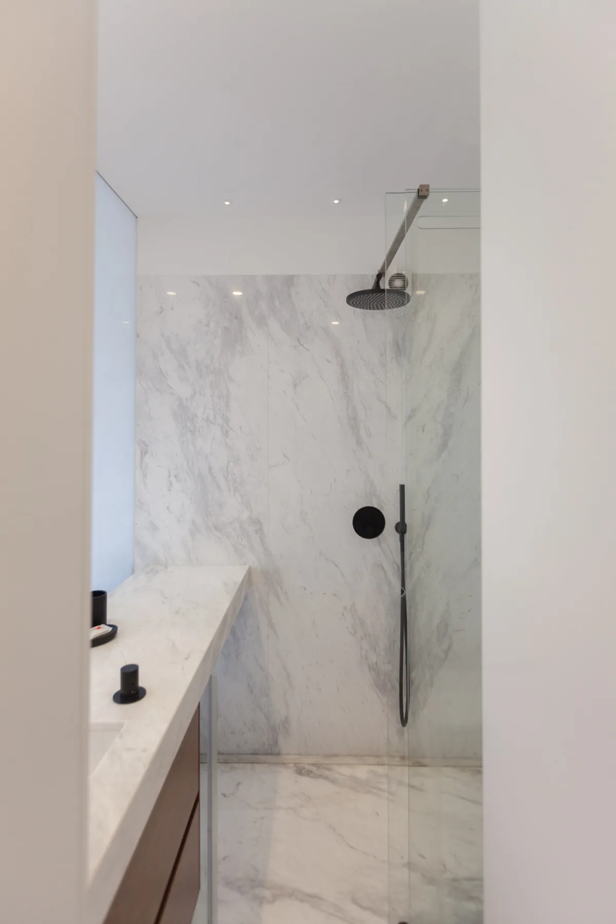 Zona de ducha en un baño con una amplia alcachofa superior y paredes claras veteadas.