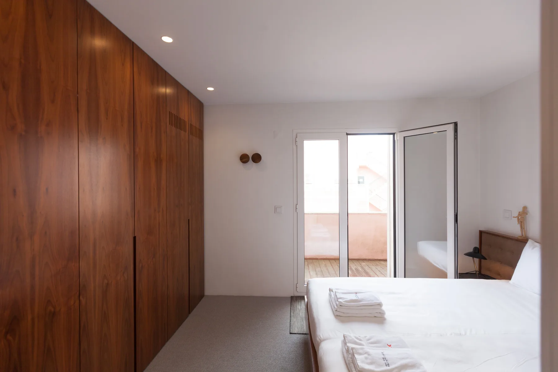 Un dormitorio con una cama junto a armarios de madera y puertas abiertas a un balcón.
