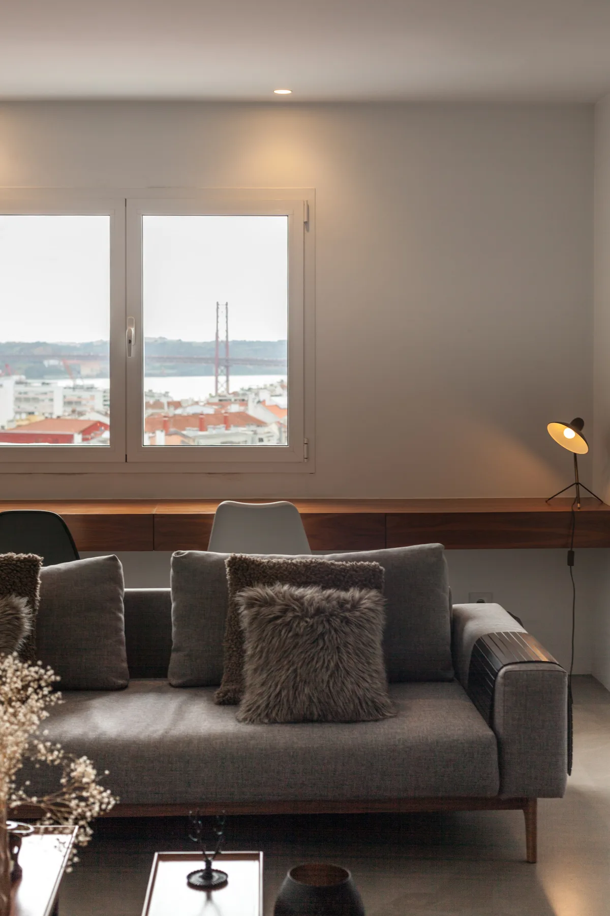 Una sala de estar con asientos grises junto a una ventana amplia con vistas a la ciudad y al río.