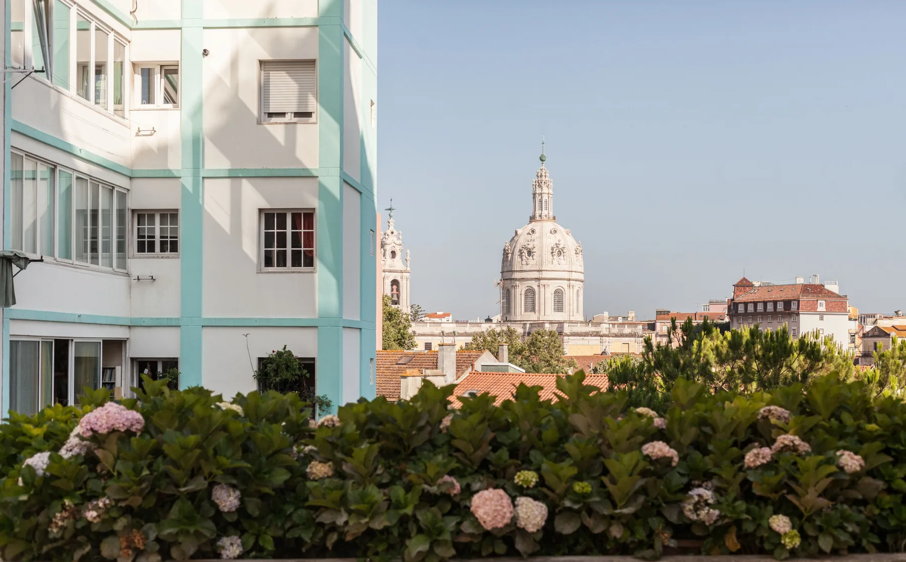 Un paisaje urbano con un edificio con cúpula, detrás de un seto y junto a edificios de apartamentos.
