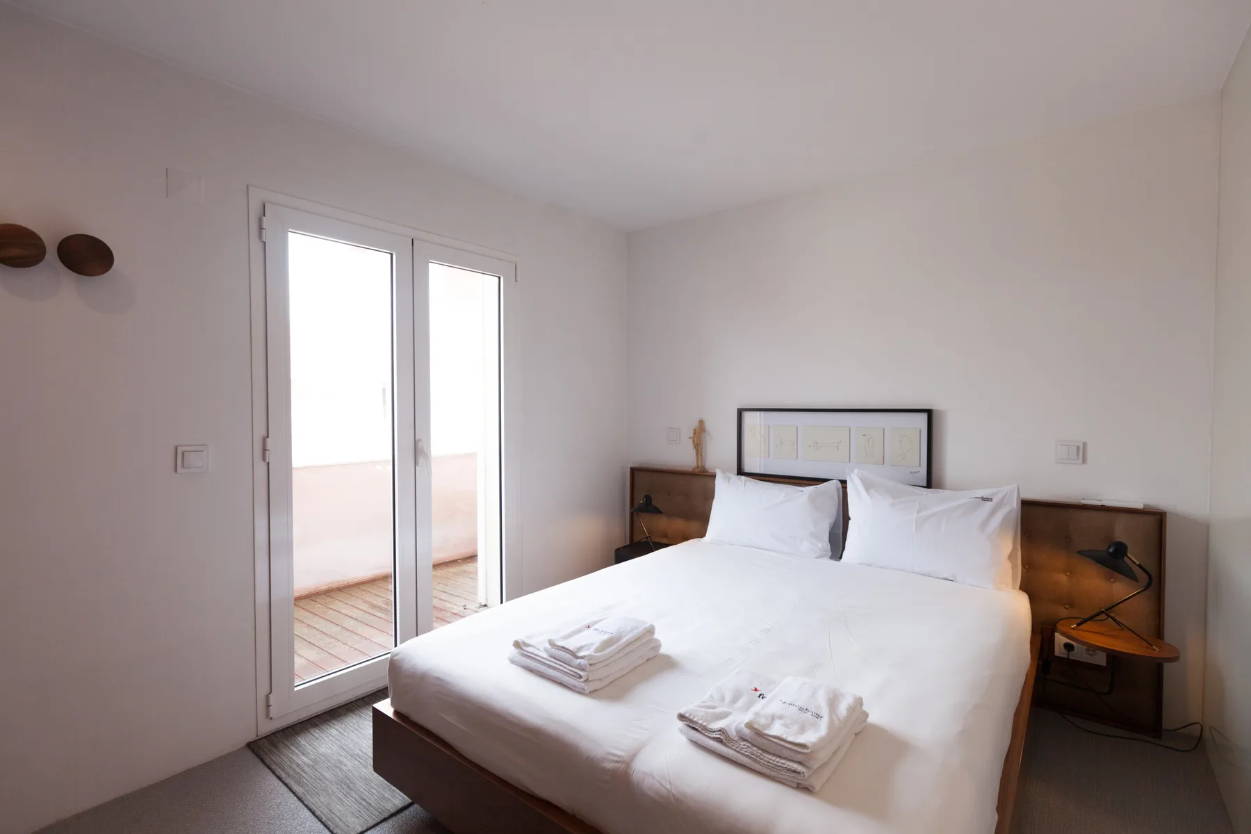 Un dormitorio con una cama bien tendida y puertas de vidrio que dan a un balcón.