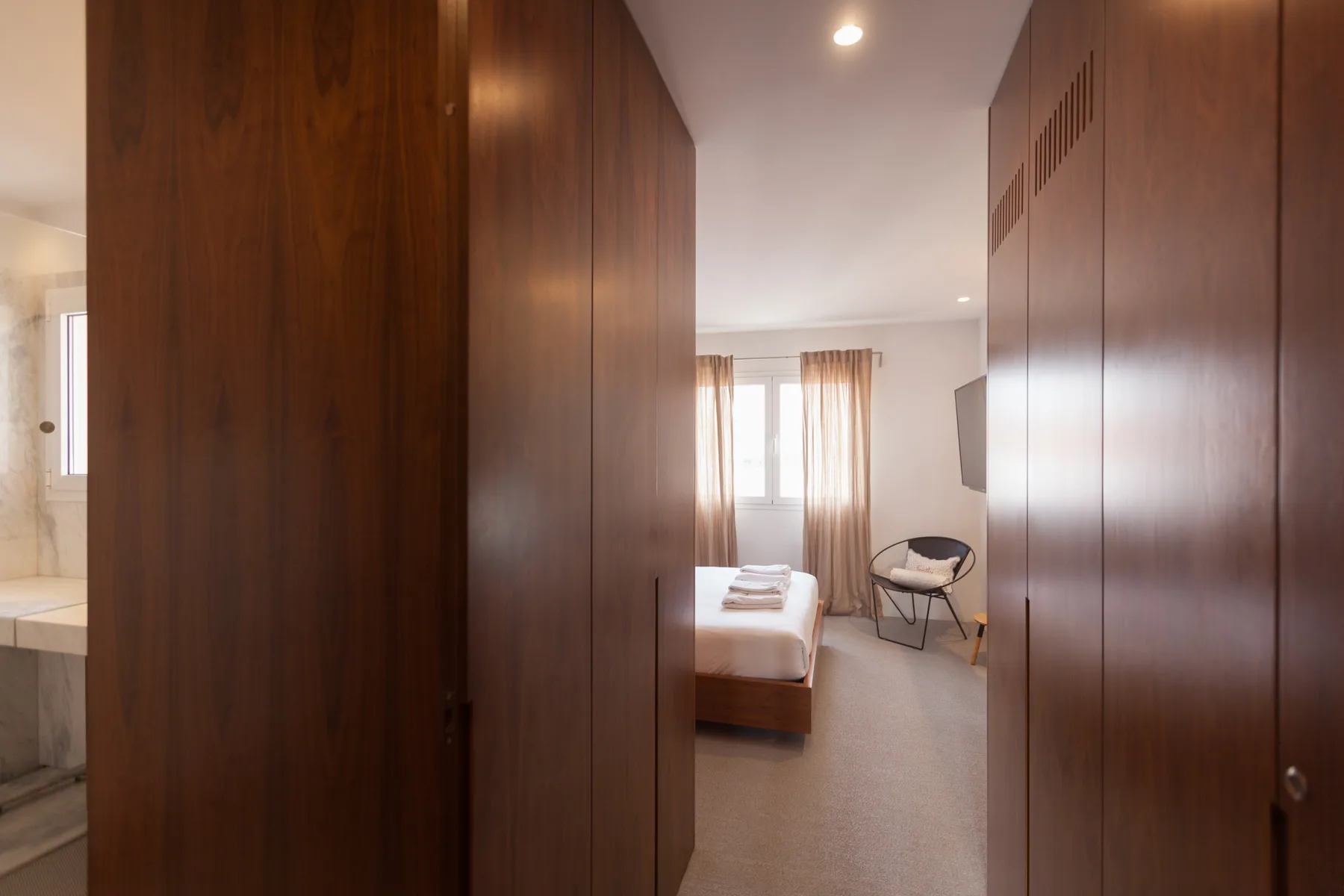 Se ve un dormitorio al fondo de un pasillo con armarios de madera.