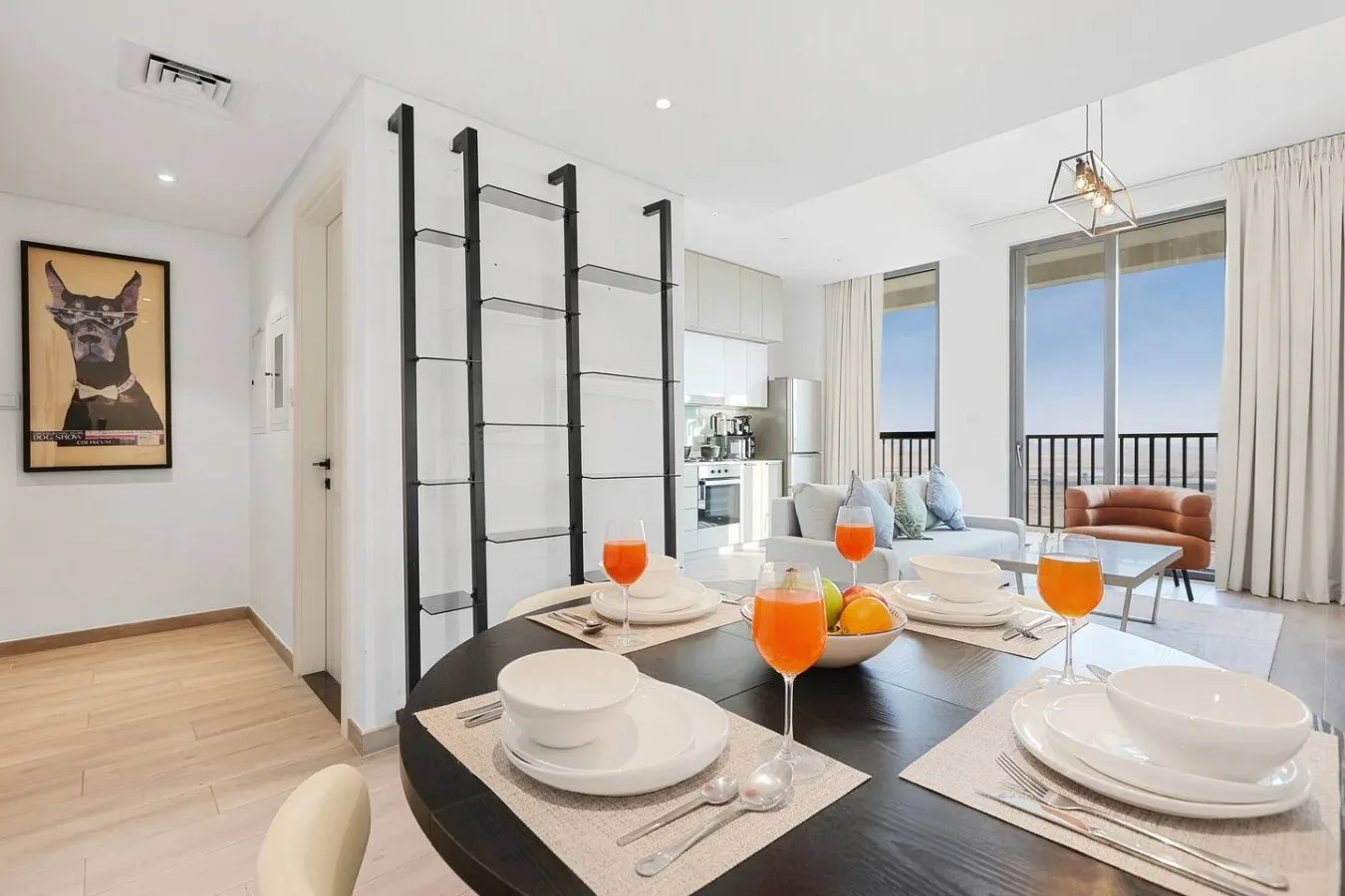 Una mesa de comedor en una sala luminosa y abierta, con cocina y zona de estar al fondo.