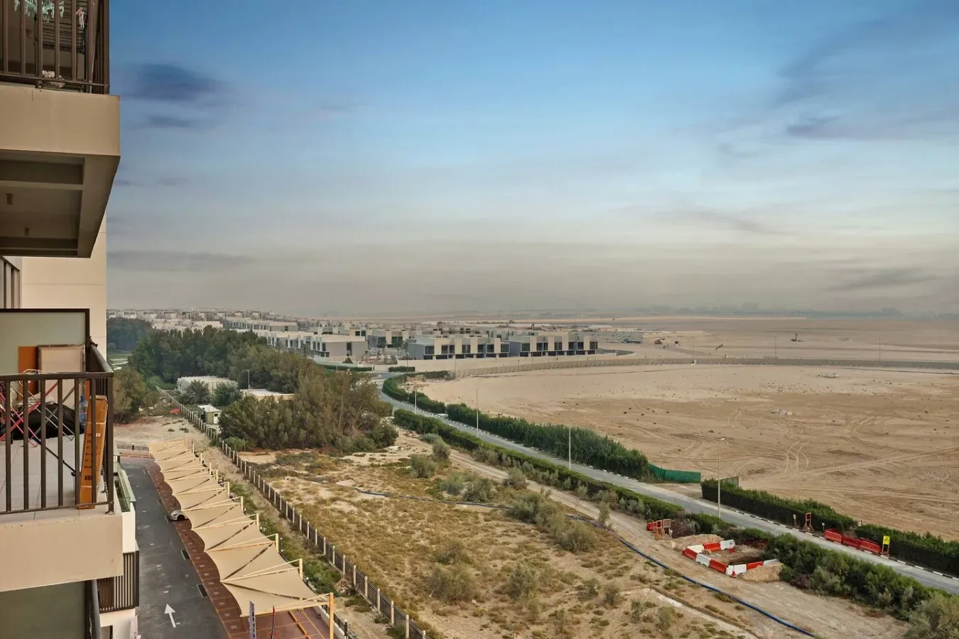 Un balcón da a un paisaje árido con una carretera y edificios a lo lejos.