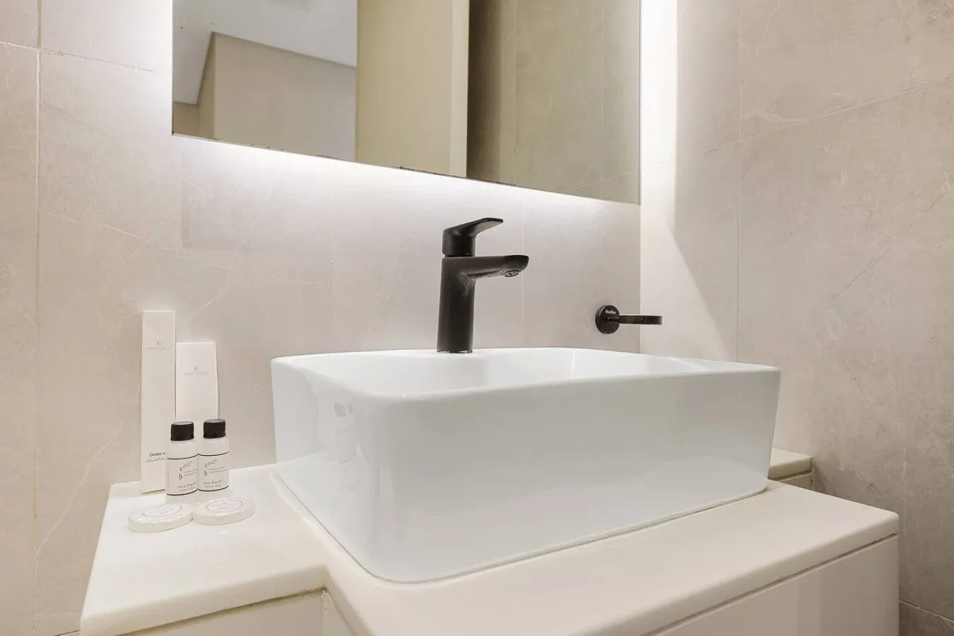 Un tocador de baño con lavabo blanco sobre encimera, grifo oscuro y espejo.