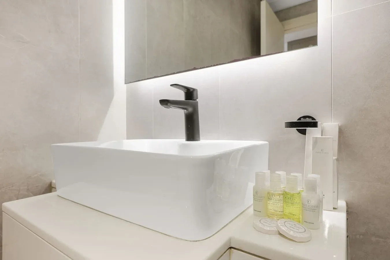 Un tocador de baño luminoso con lavabo blanco, grifo oscuro y artículos de aseo.
