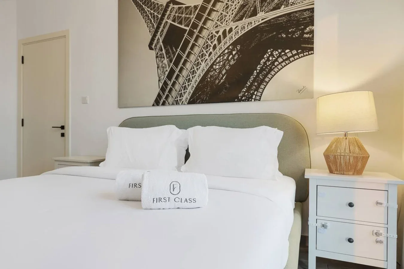 Un dormitorio con una cama tendida, almohadas blancas y una lámpara de noche.