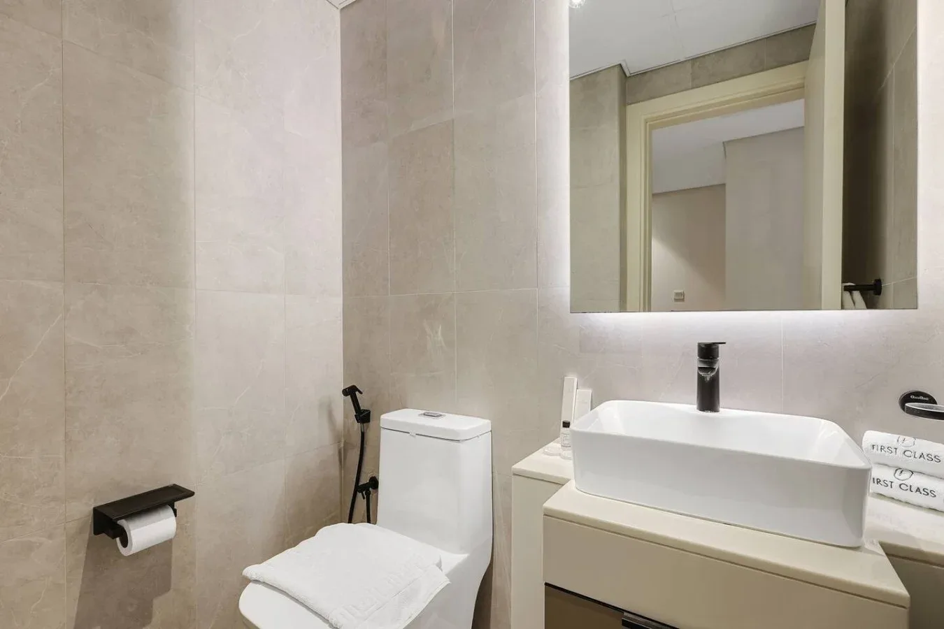 Un baño con azulejos, lavabo, espejo, inodoro y toallas dobladas.