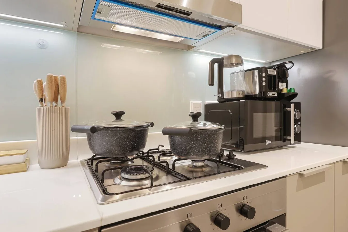 Una cocina luminosa con una placa de gas, ollas y electrodomésticos sobre la encimera.