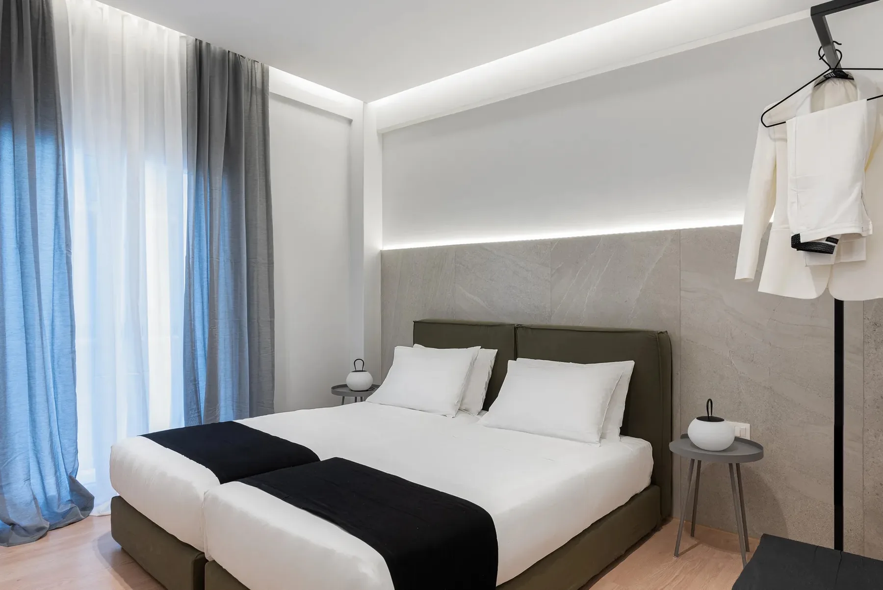 A bedroom with a double bed, white linens, and curtains by the window.