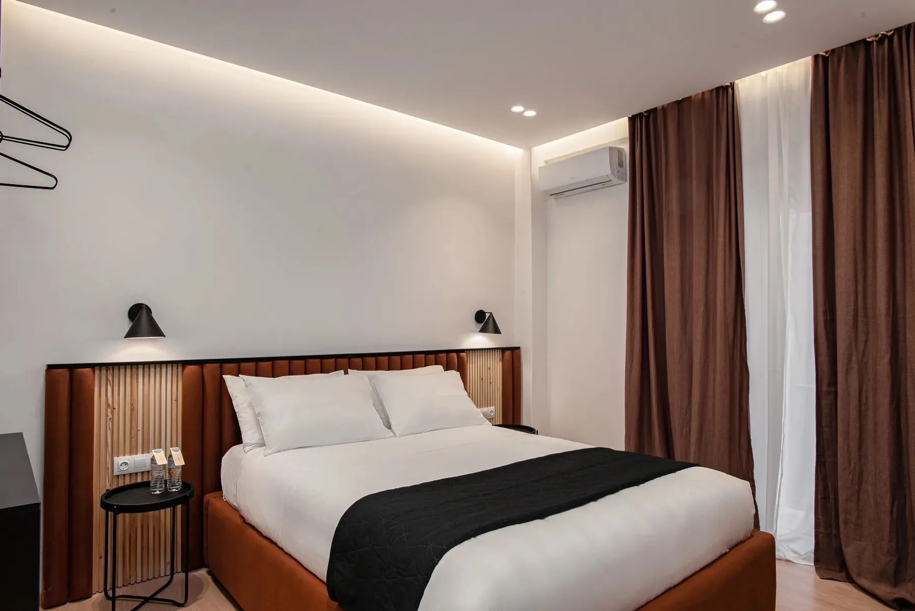 A bedroom with a bed, bedside tables, and floor-length curtains.