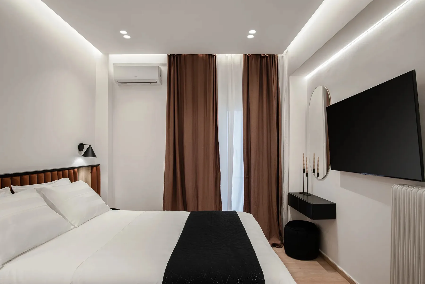 Dormitorio con una cama tendida y un televisor montado en la pared.