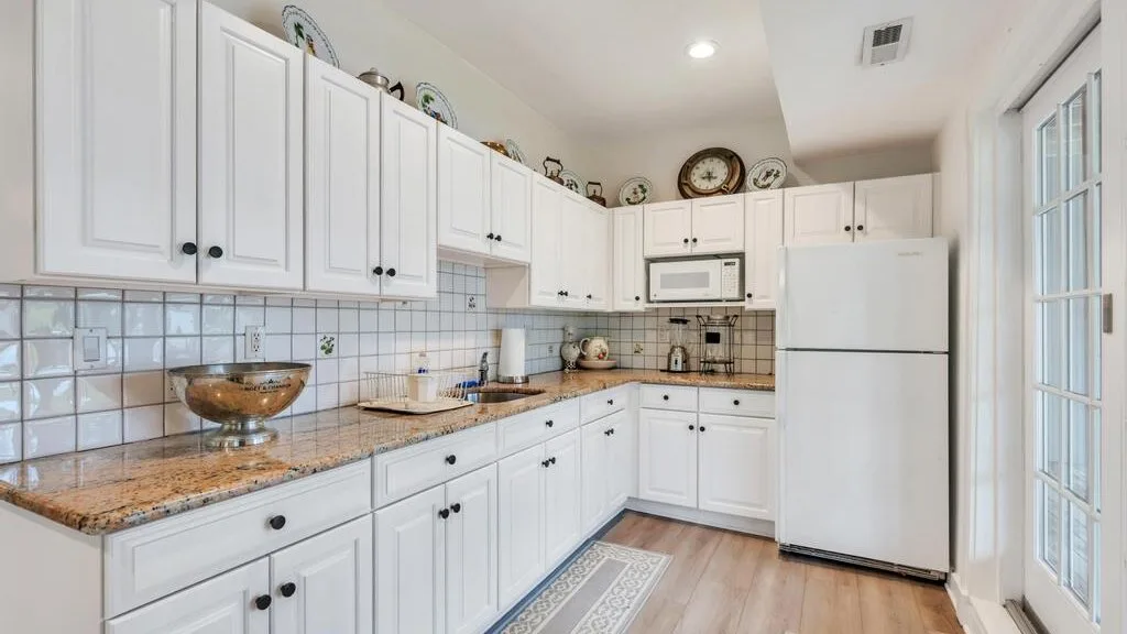 Una cocina luminosa con gabinetes blancos, azulejos decorados y un refrigerador.
