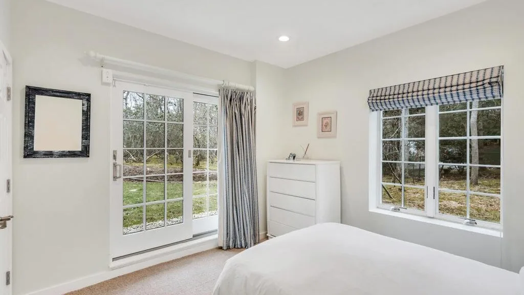 Un dormitorio luminoso con una cama junto a ventanas grandes y una puerta de vidrio.