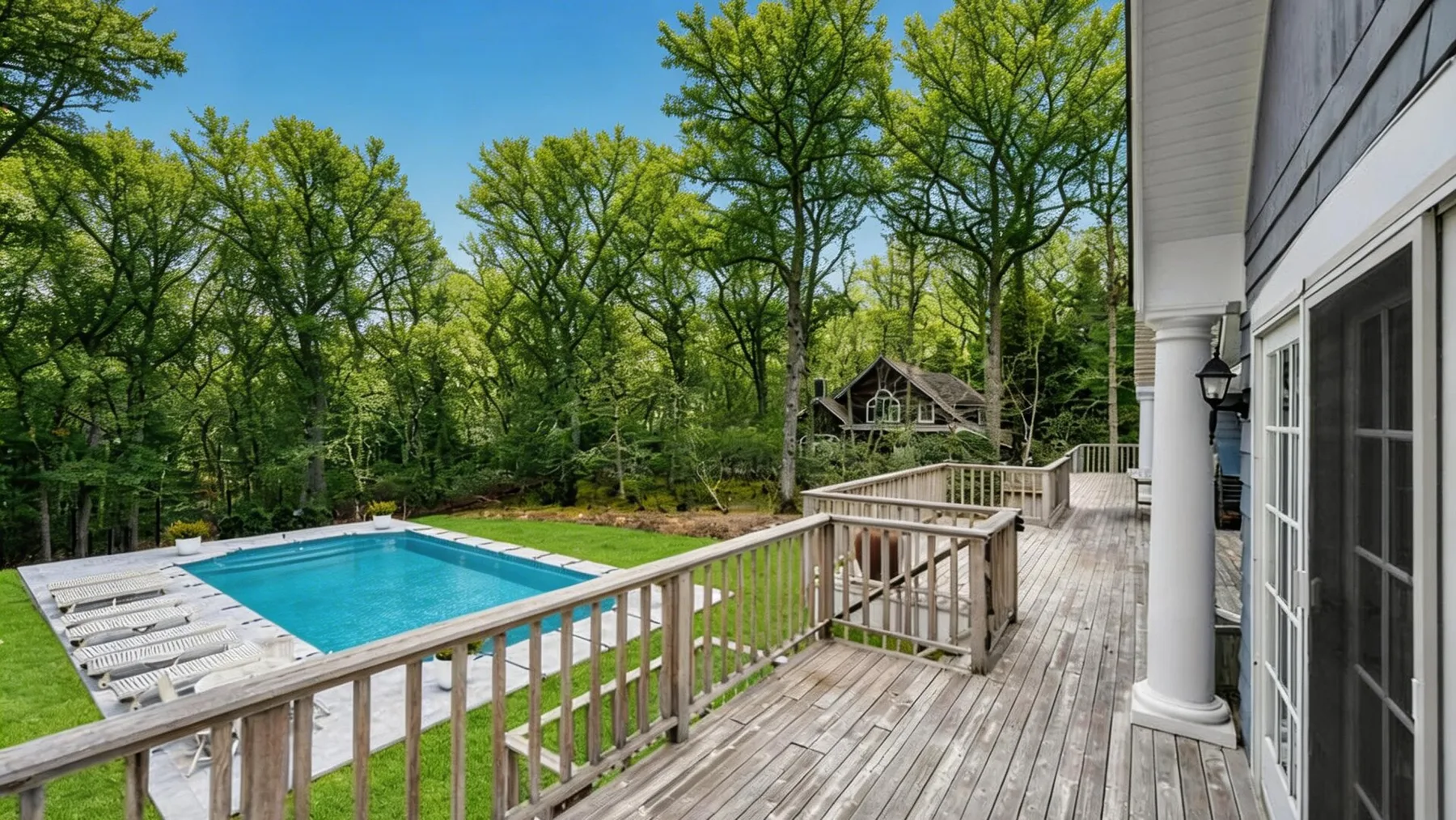 An outdoor deck overlooks a swimming pool surrounded by trees.