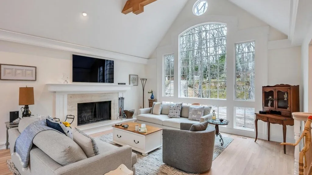 A bright living room with seating arranged around a fireplace and large windows.