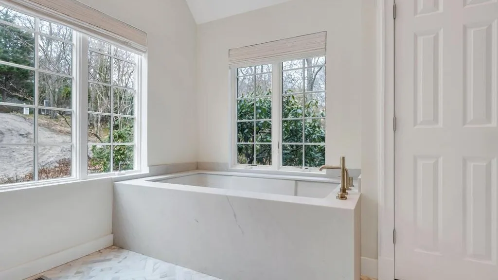 Un baño luminoso con una bañera junto a grandes ventanas.