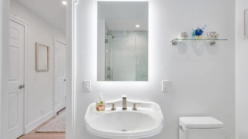 Un baño luminoso con lavabo, espejo de pared y ducha de vidrio.