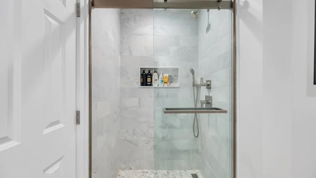 Una ducha de baño con azulejos, paneles de vidrio y un estante en la pared.