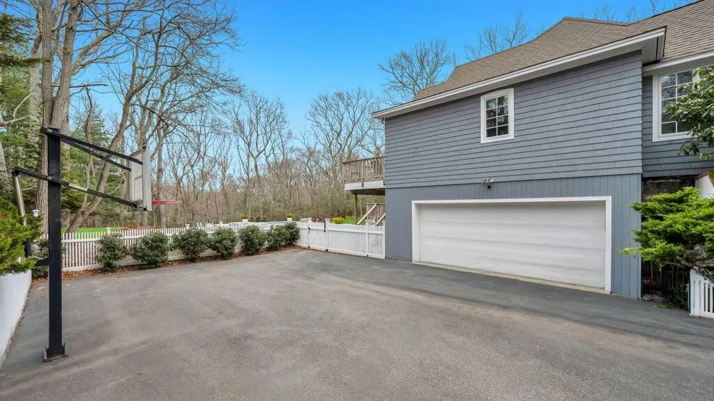 Una entrada pavimentada junto a una casa gris con una puerta de garaje blanca.